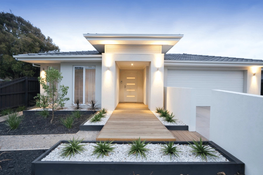 white contemporary style home with garage, plants, and exterior lighting